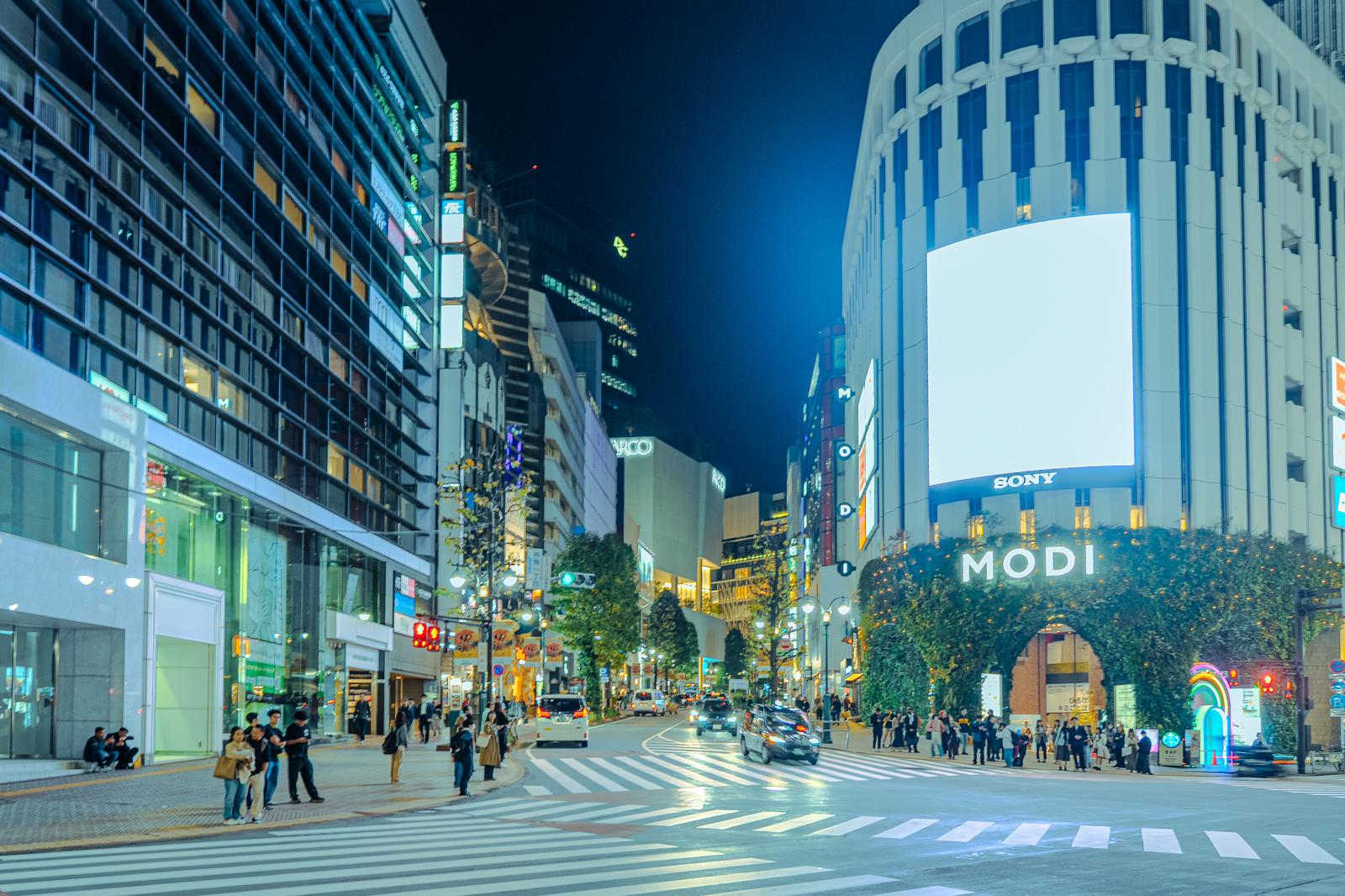 夜間に撮影した渋谷MODI前の交差点。高層ビルに囲まれ、多くの人が横断歩道を渡っている