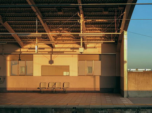夕暮れ時の駅のホームに並ぶ椅子と金色の光