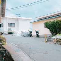 坂道の道路脇に並ぶ2台のスクーターと集積所の写真