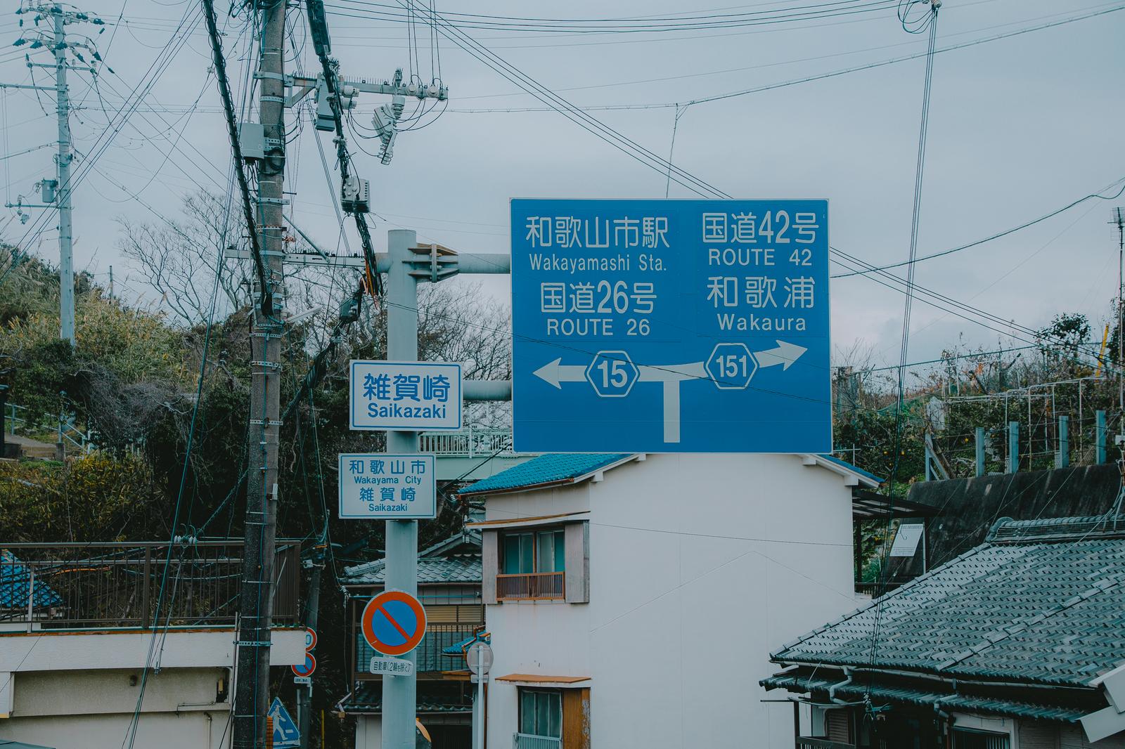 和歌山県雑賀崎の交差点に立つ青い道路標識と周囲の町並み