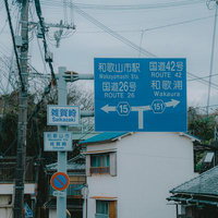 和歌山の雑賀崎交差点に立つ青い道路標識と町並みの写真