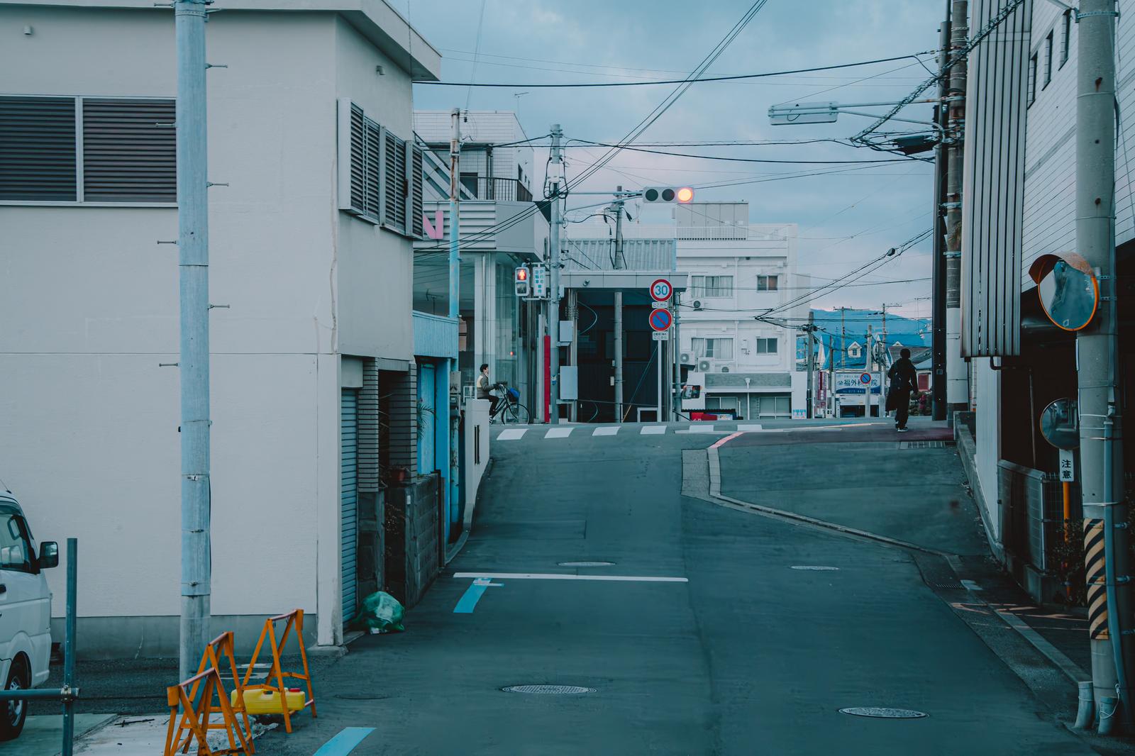 坂道の先の交差点で赤く灯る信号機。白い建物と電線が見える日本の路地