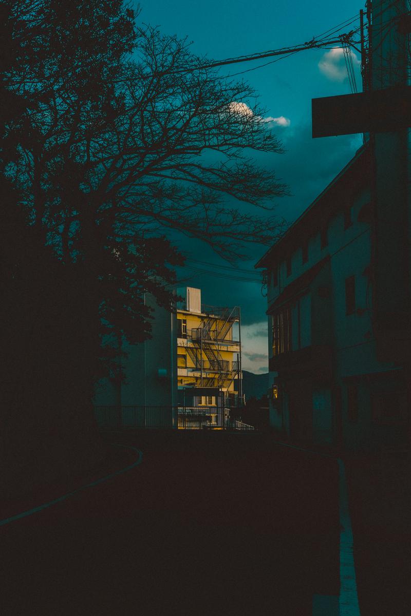 夜が迫る中、黄色い建物が浮かぶ路地の風景
