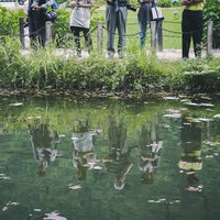 水面に反射する池の前に立つカメコを持つ観光客の姿の写真