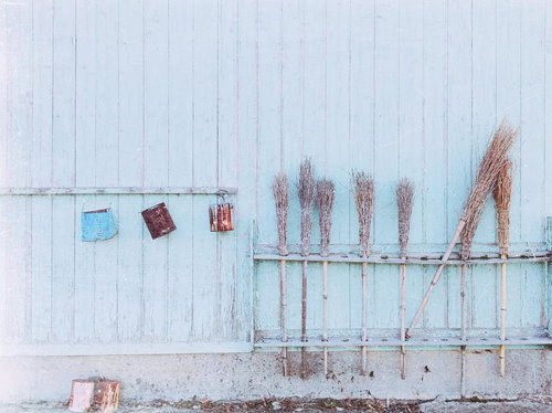 ペンキが剥がれた壁に掛けられた箒や古い道具