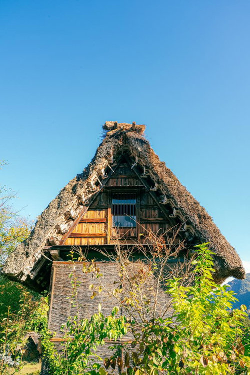 合掌造りの茅葺き屋根と木製の階段窓・富山県南砺市の伝統民家