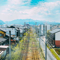 住宅街の中心を走る線路と遠くの山並み、電柱と架線の写真