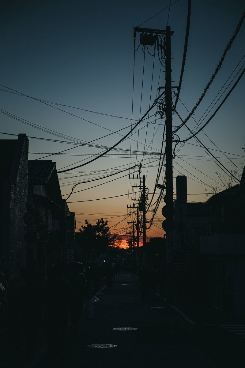 夕暮れ時の住宅街で電線と電柱のシルエットが夕焼け空に映る
