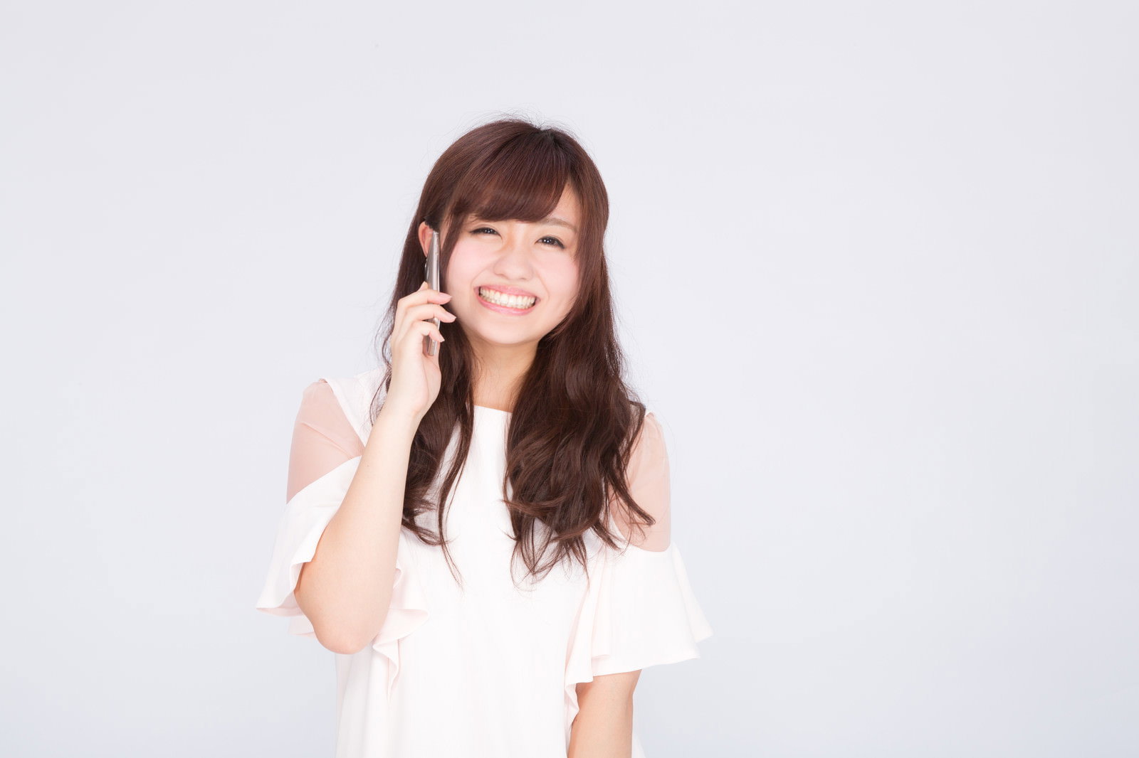 白い服を着た女性がスマートフォンで通話しながら笑顔を見せている［モデル：河村友歌］