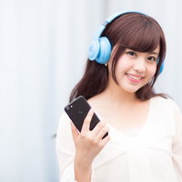 ブルーのワイヤレスヘッドフォンで音楽を楽しむ女子の写真