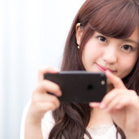 ブラック色のスマートフォンで撮影する笑顔の女性の写真