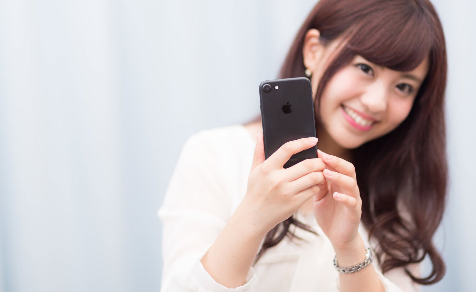 黒いiPhoneを両手で持つ笑顔の女性［モデル：河村友歌］
