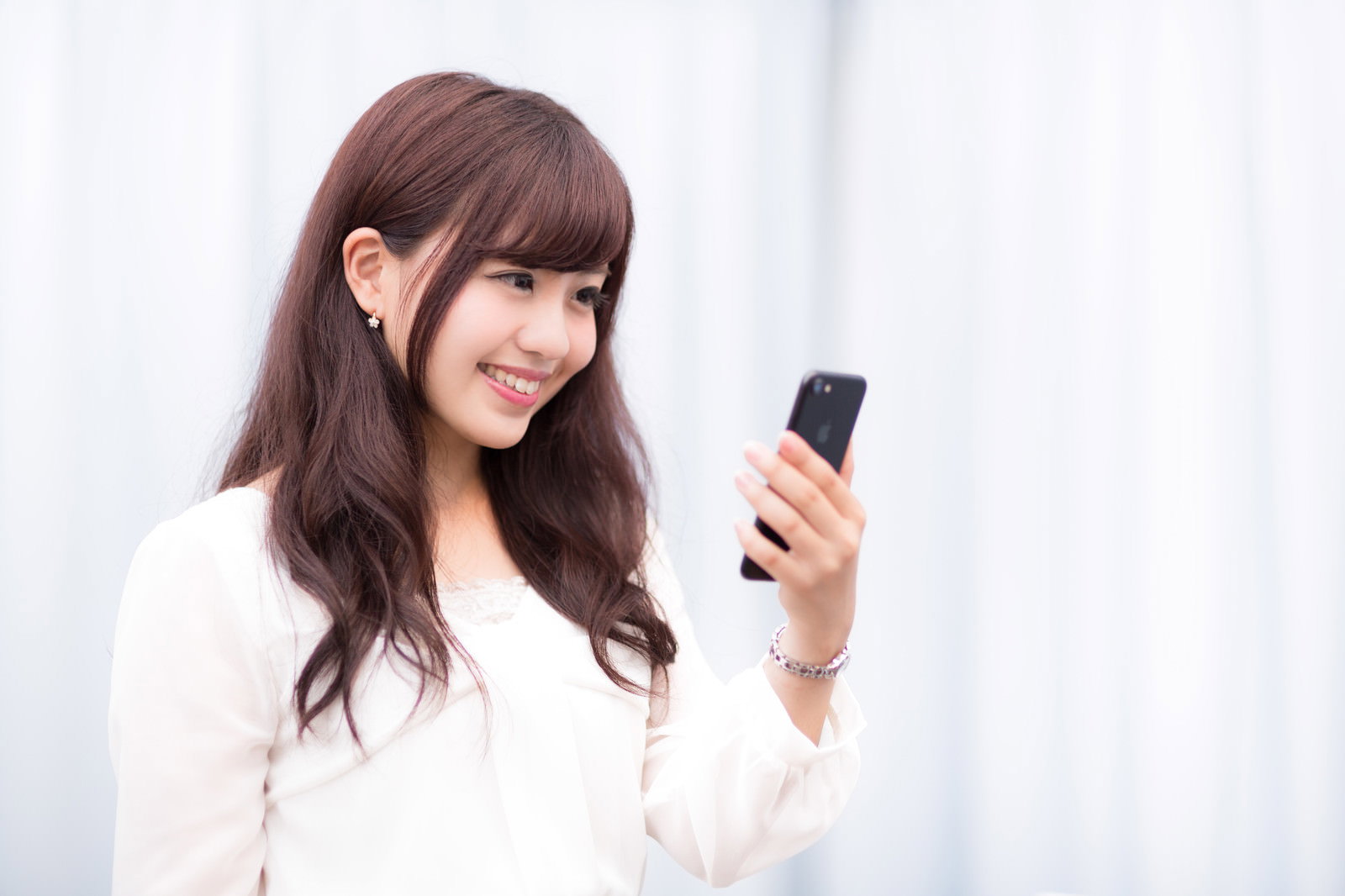 スマホを見て笑顔の長髪女性［モデル：河村友歌］