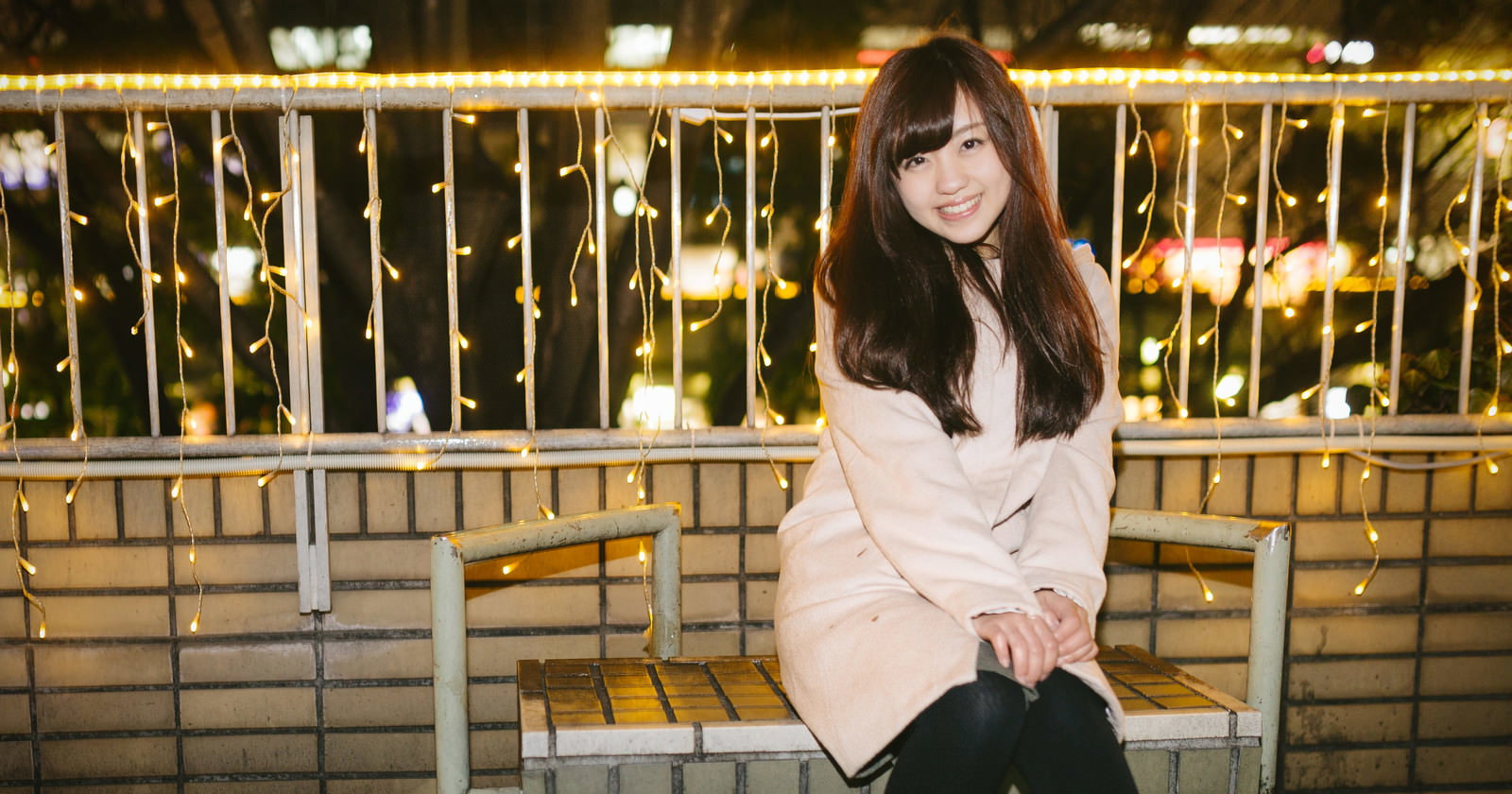 夜の繁華街でイルミネーション前のベンチに座る女性［モデル：河村友歌］