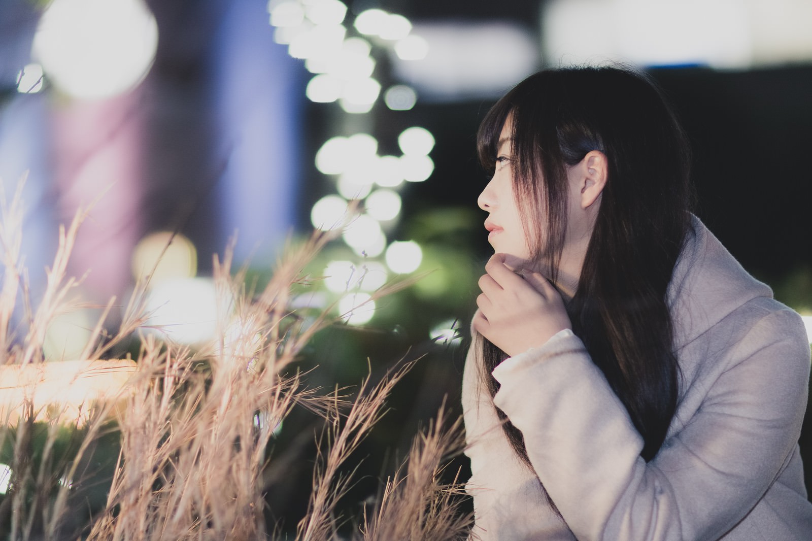 夜景の玉ボケを背景に、悩みながら遠くを見つめる女子大生［モデル：河村友歌］