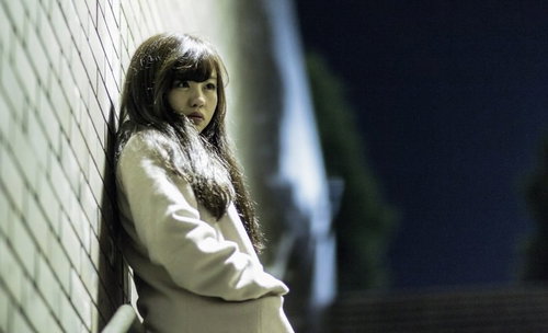 チャンスを逃して放心状態の女性、白いコートを着て壁に背を向けて立つ