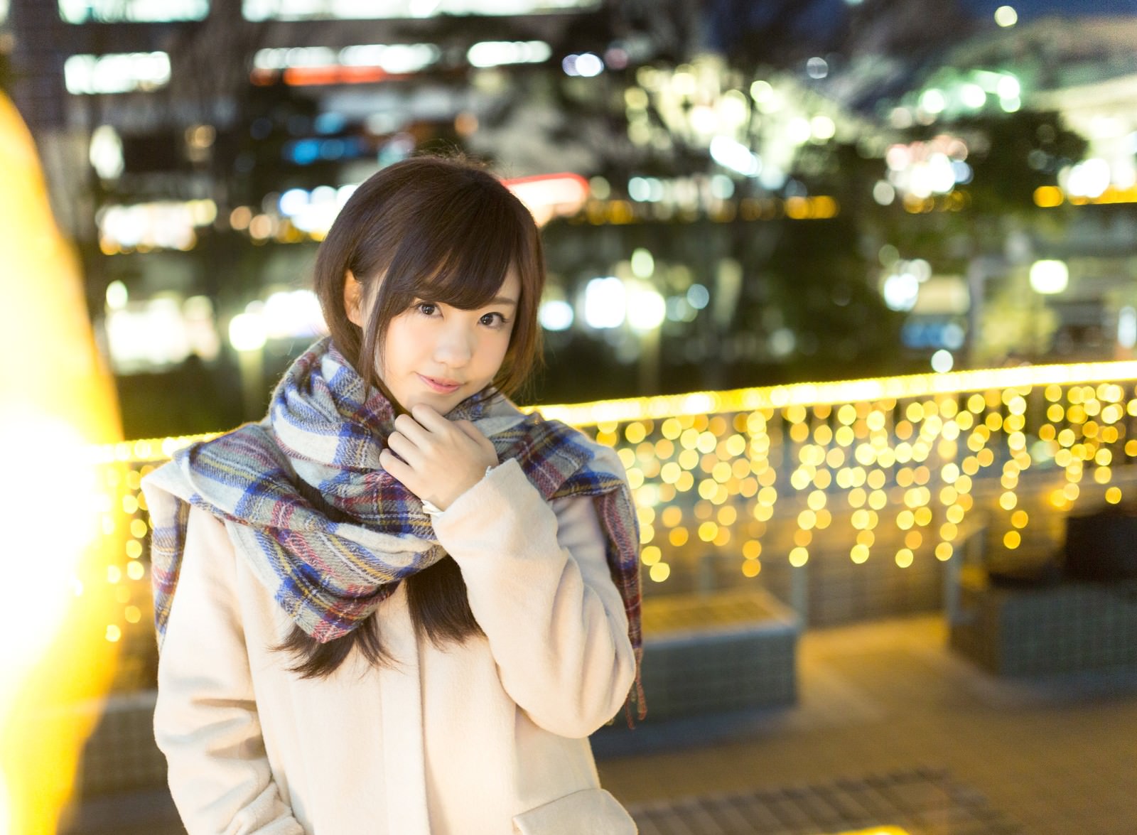 イルミネーション前でチェック柄マフラーを巻いて微笑む女性［モデル：河村友歌］