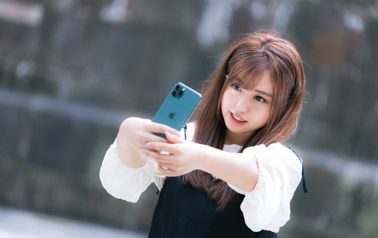 iPhone 11 Proを持って自撮りする白いトップスの女性［モデル：河村友歌］