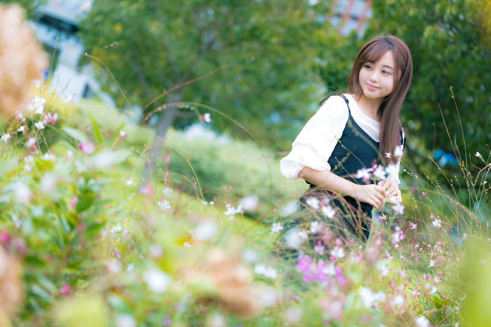 白い服を着た女性が緑豊かな花壇の前でしゃがんでいる様子［モデル：河村友歌］