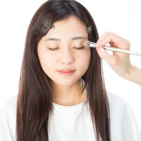 メイクブラシでアイシャドウを入れるメイク中の女性の写真