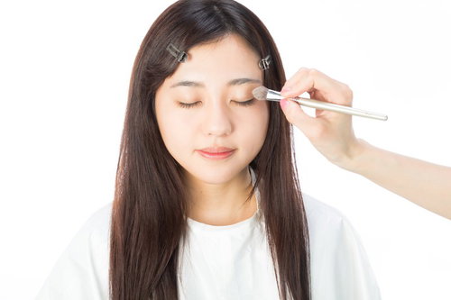 メイクブラシでアイシャドウを入れるメイク中の女性