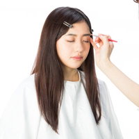 メイクアップアーティストに眉毛を描いてもらう女性の写真