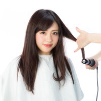 ヘアアイロンで毛先を巻く女性の美容施術の写真
