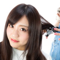 美容師がヘアアイロンで髪を巻いてもらう女性の写真