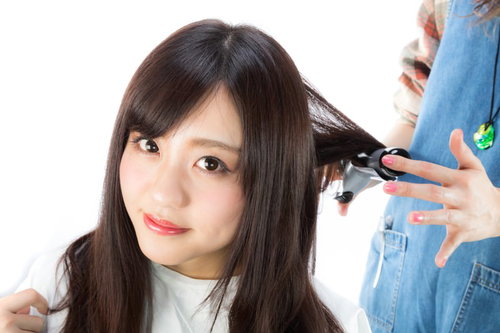 美容師がヘアアイロンで髪を巻いてもらう女性