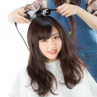 サロンモデルの髪の根元をヘアアイロンで巻く美容師の写真