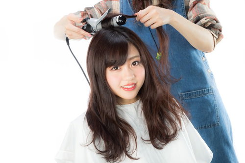 サロンモデルの髪の根元をヘアアイロンで巻く美容師