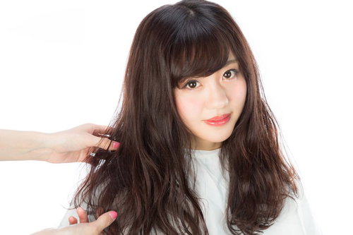 巻いた髪に整髪剤をつける美容師とモデルのヘアスタイリング