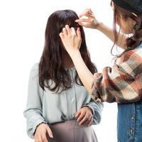 撮影現場でモデルのヘアメイクを手直しする美容師の写真