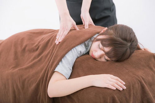 整体の施術中に眠ってしまう女性、背中をほぐす施術者の手