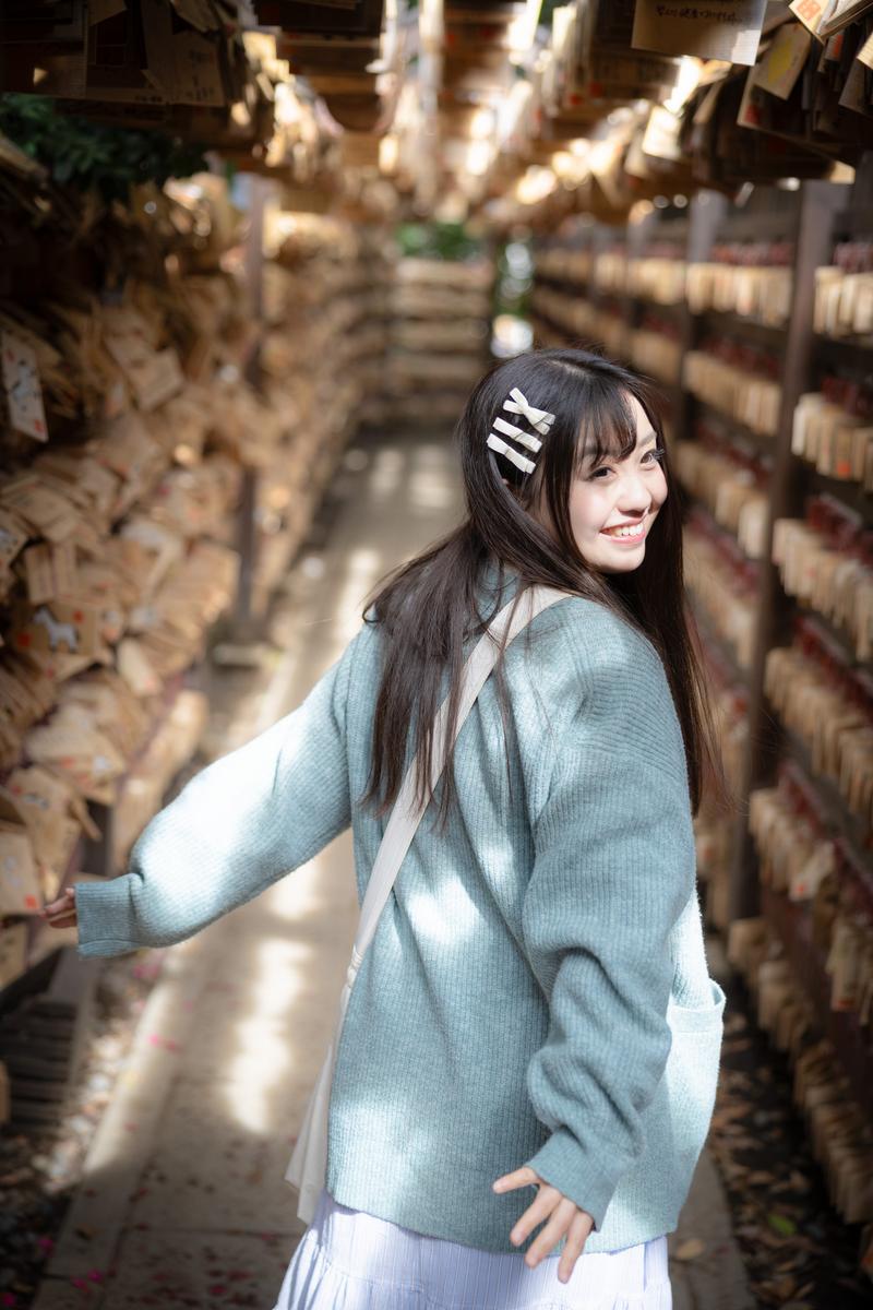 Young woman smiling among ema votive plaques at a Japanese shrine corridor