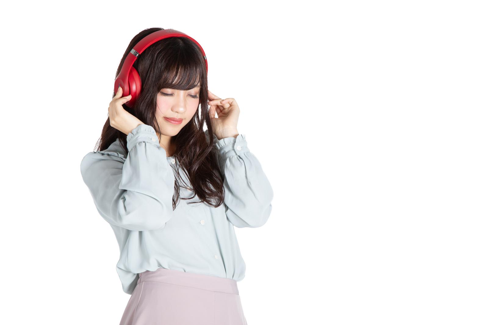 赤いヘッドフォンをつけて目をつぶり、音楽を聴く女性［モデル：河村友歌］
