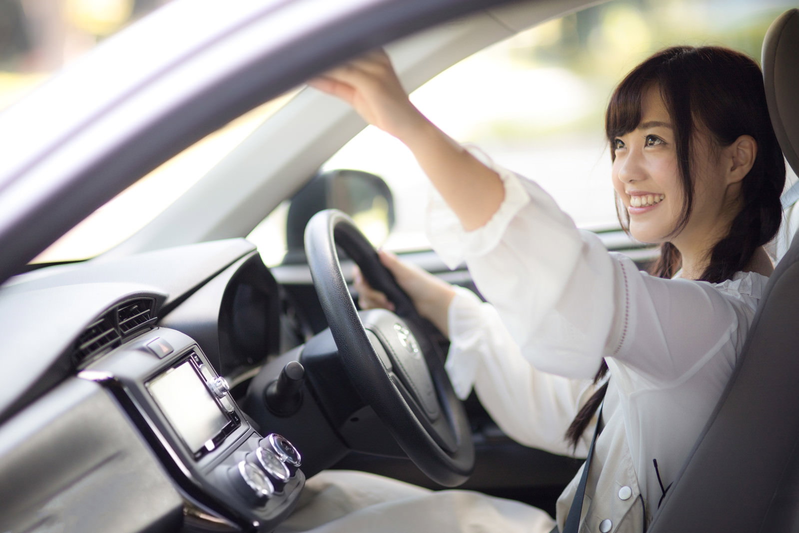 運転席でバックミラーを調整する女性ドライバー［モデル：河村友歌］