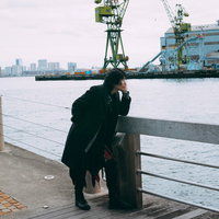 港の柵に寄りかかって夕方の海を眺める男性の後ろ姿の写真