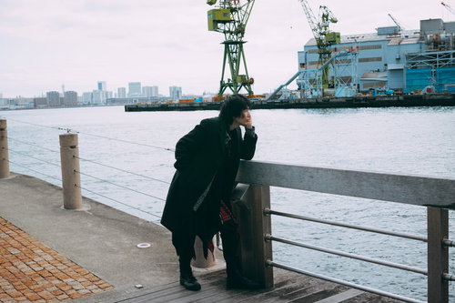 港の柵に寄りかかって夕方の海を眺める男性の後ろ姿