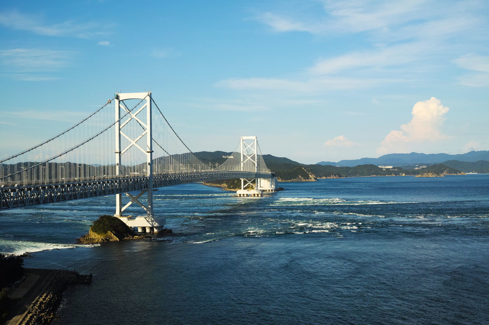 青い鳴門海峡に白い渦潮が巻き、上空に大鳴門橋が架かる風景