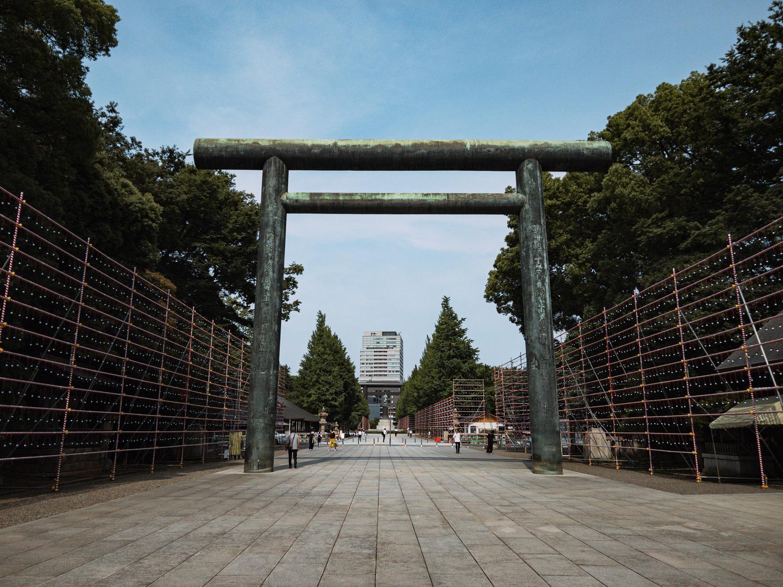 靖国神社の参道入口に立つ大きな鳥居と左右に続く赤茶色の柵