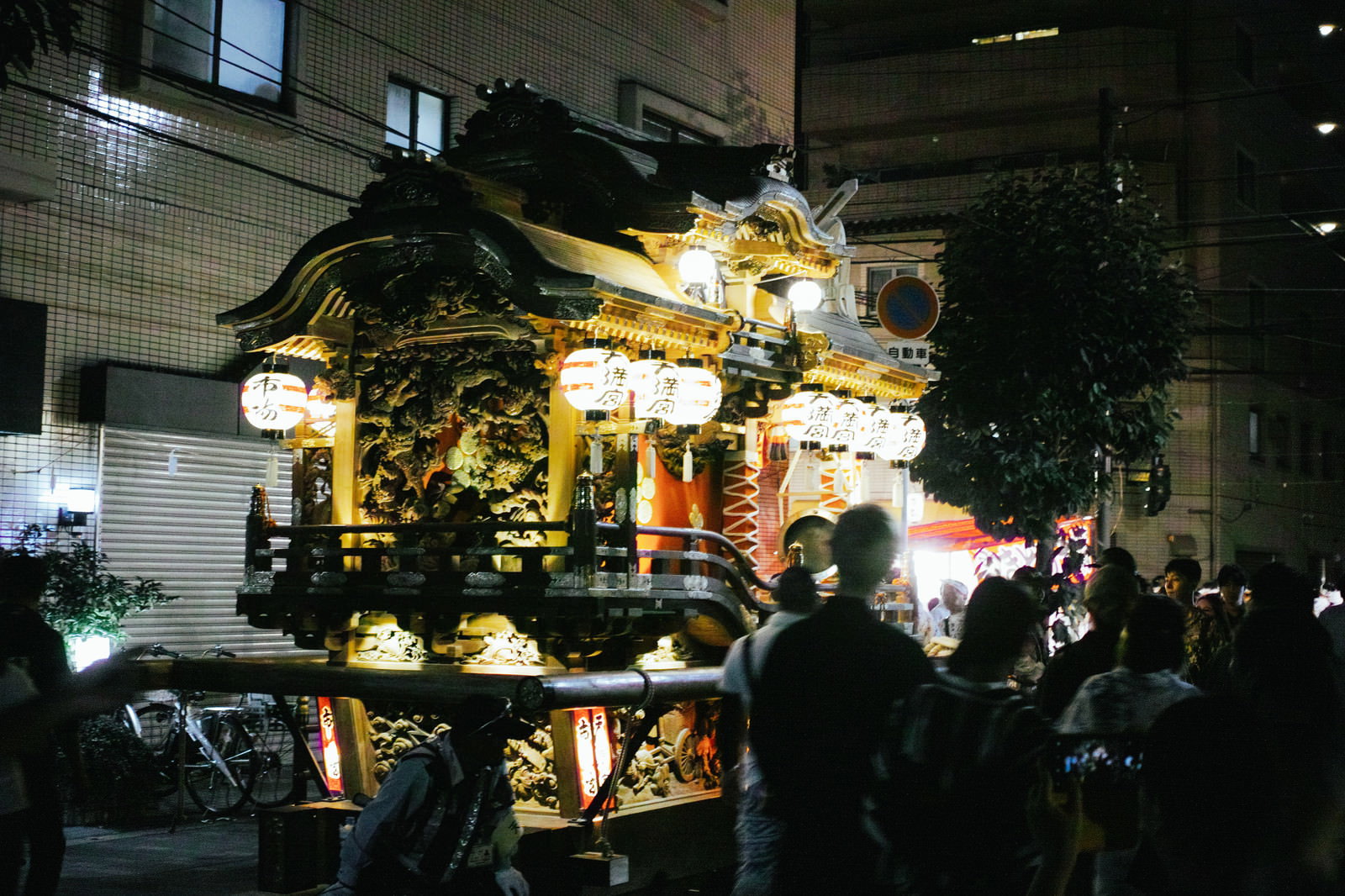 夜の祭りで担がれる御輿と周囲の屋台、提灯の明かりと人々