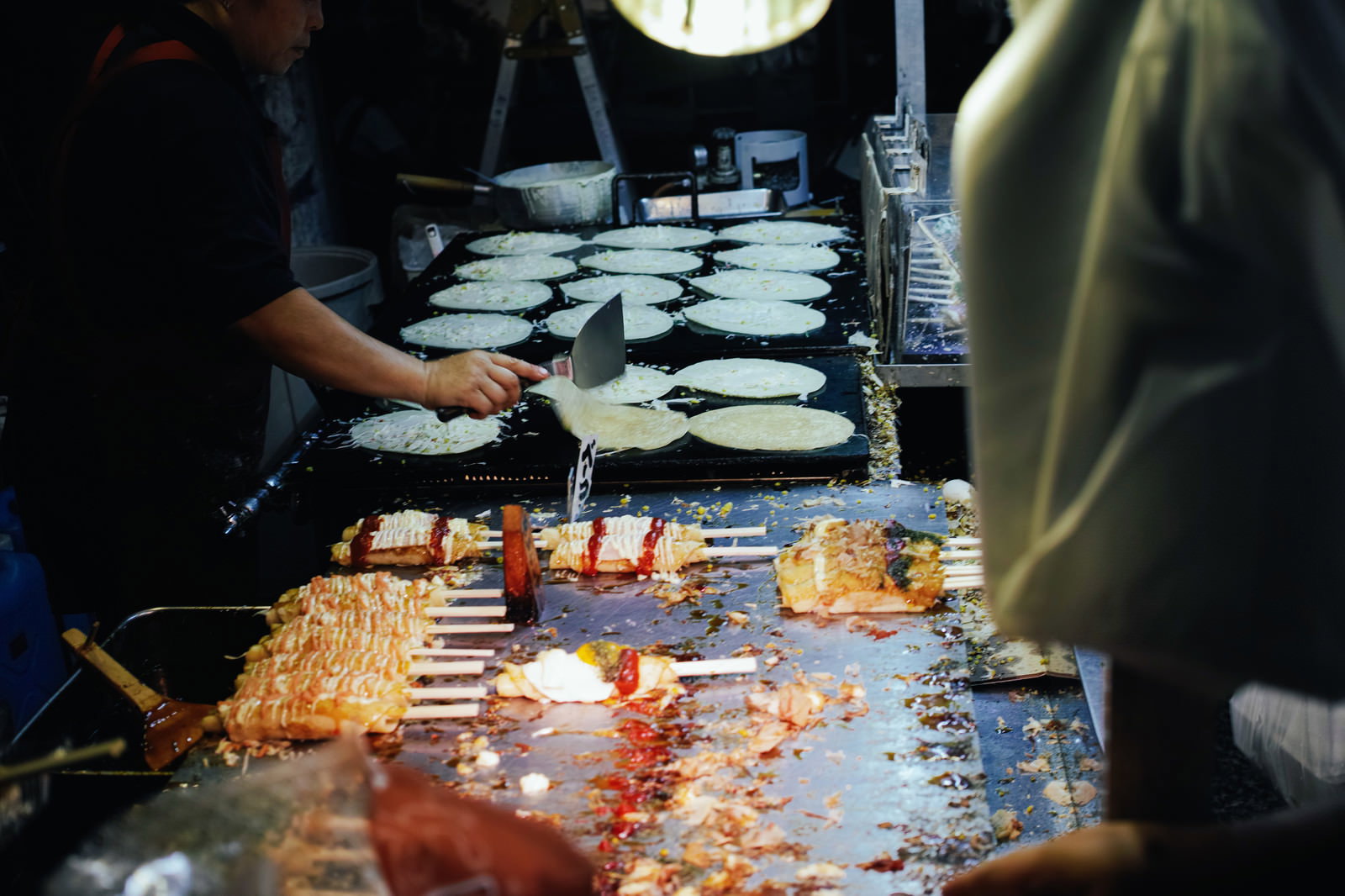 夜の屋台で複数のフライパンを使ってお好み焼きを焼いている様子