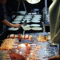 露天の的屋で焼かれるお好み焼きの写真