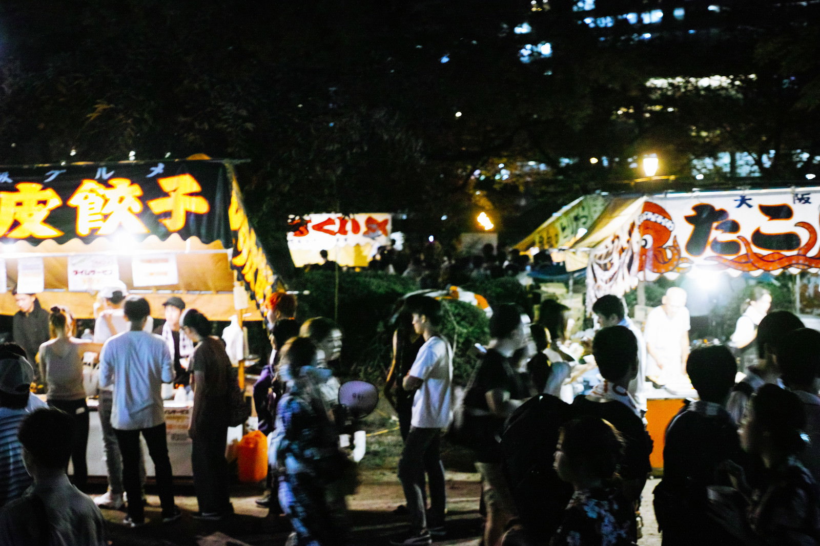 提灯の明かりが灯る夜の屋台街で人々が行き交う賑やかな風景
