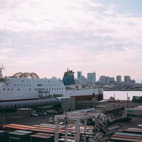 港の埠頭に停泊する大型船とコンテナ、遠くに見えるビル群の写真