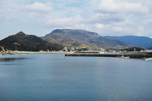遠くの山と波止場に停泊する複数の船が並ぶ港町の風景