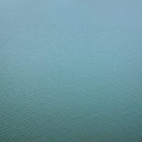 青緑色に輝く穏やかな海の水面と微細な波紋の写真