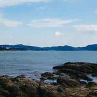 穏やかな海と遠くに見える山、手前の岩場が広がる海岸風景の写真