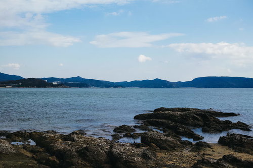 穏やかな海と遠くに見える山、手前の岩場が広がる海岸風景